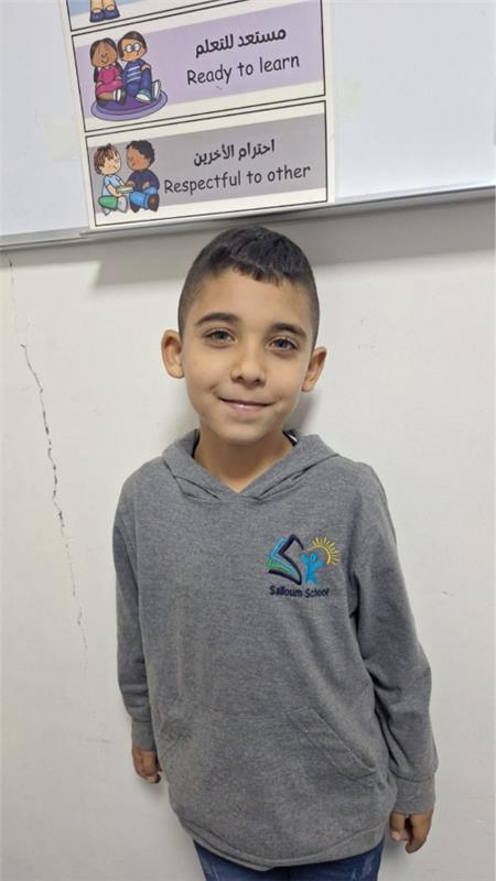 Ali, age 7, from Nabatieh, smiling in his school hoodie in front of a classroom wall
